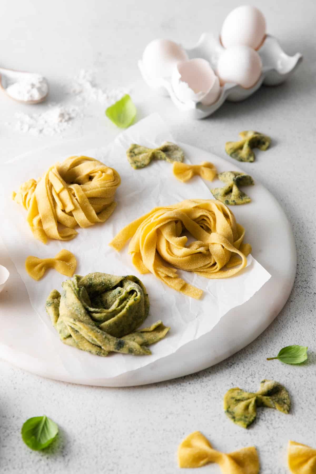 close up of 3 nests of homemade pasta on a round marble server in front of a carton of eggs.