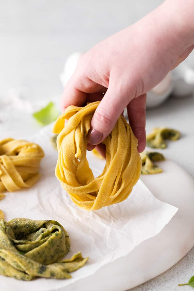 hand holding a nest of homemade pasta over a round marble server.