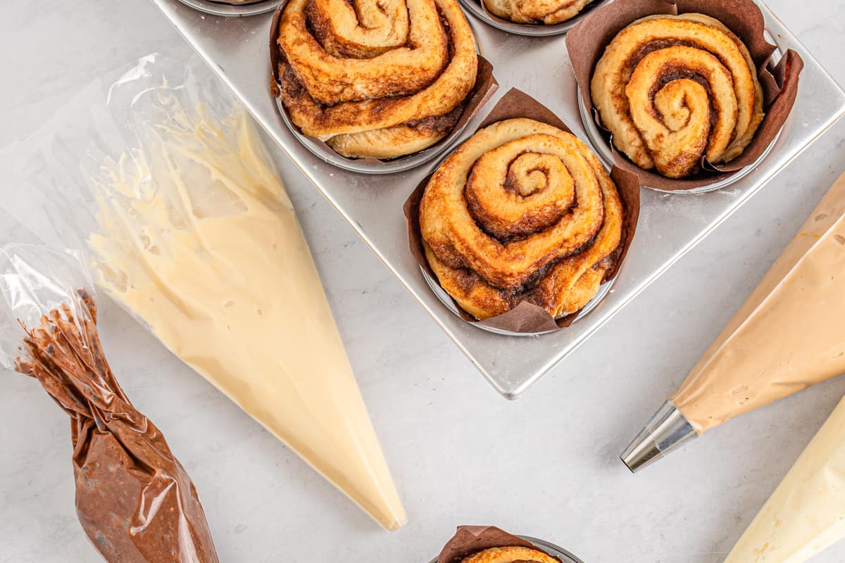 Bakery cinnamon rolls next to piping bags filled with frosting.