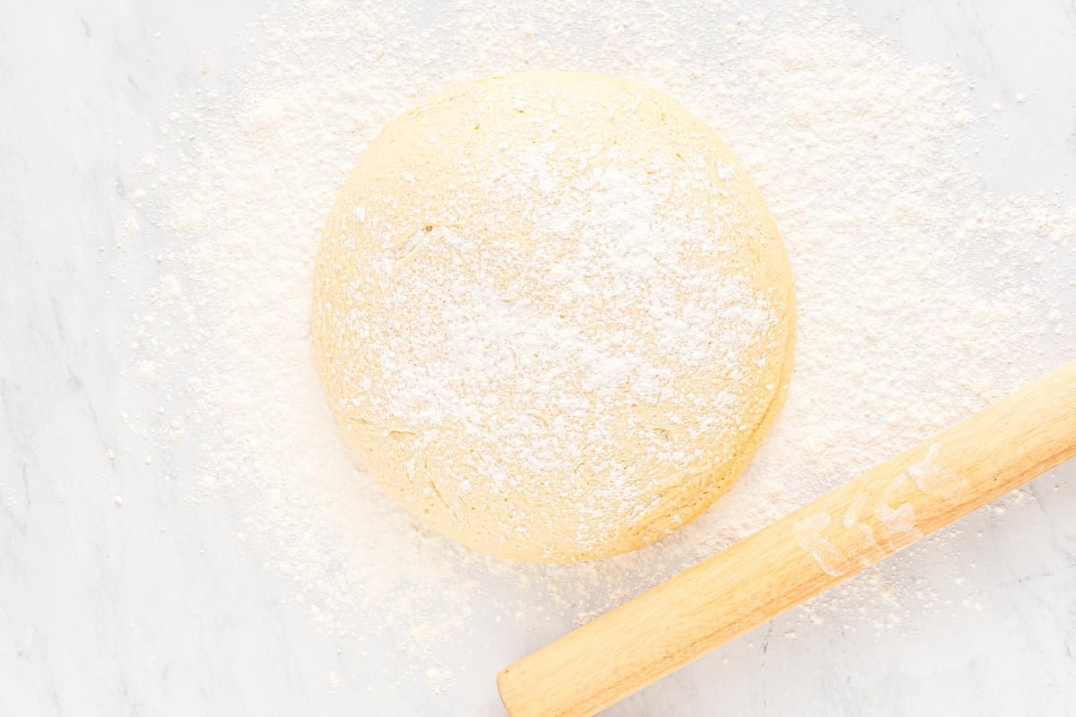 Disc of dough covered in flour, next to a rolling pin.