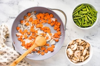 sauteed carrots and onions in a saute pan with a wood spoon