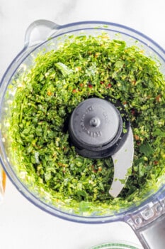 overhead view of processed herbs for grilled potato wedges with chimichurri in a food processor.