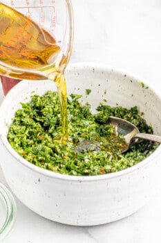 oil added to processed herbs for grilled potato wedges with chimichurri in a white bowl.