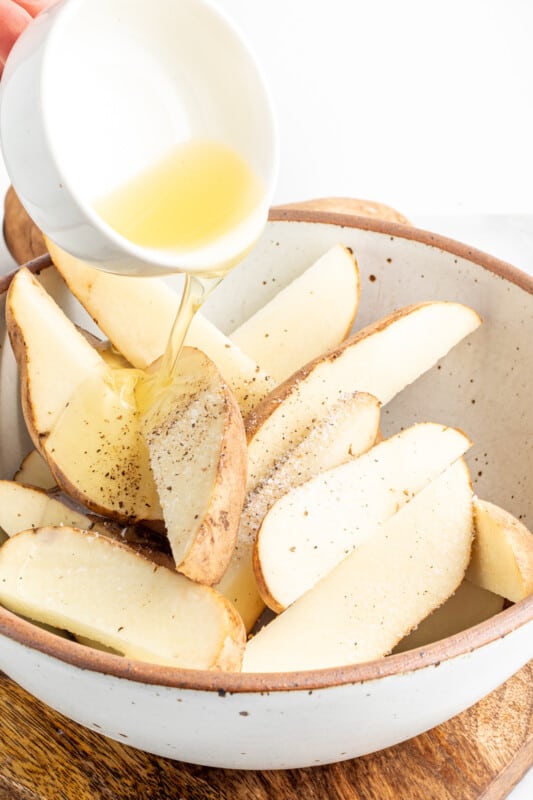 potato wedges being oiled in a white bowl.