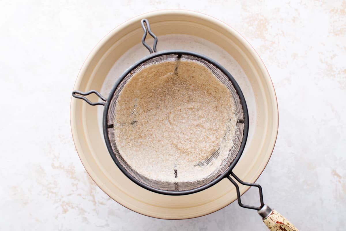 oat pulp in a fine mesh sieve over a bowl of strained oat milk.