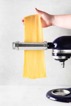 homemade pasta dough being fed through a kitchenaid pasta roller.
