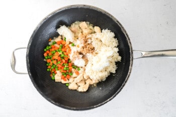 cooked chicken and onions in a wok with frozen peas and carrots and rice.