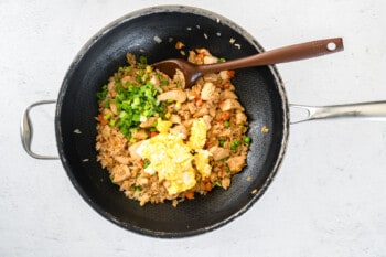 cooked chicken, vegetables, and rice in a wok with scrambled eggs and green onions.