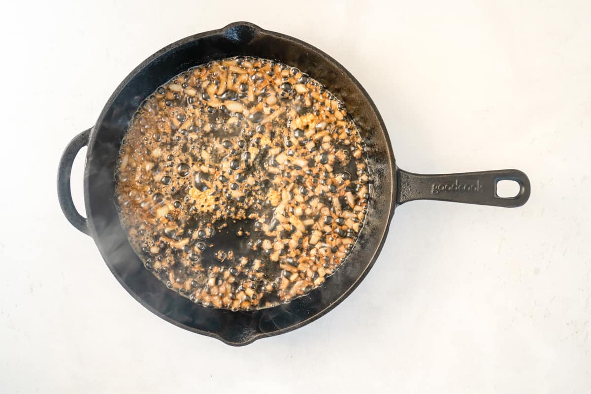 Overhead view of onions and garlic sizzling in a skillet.