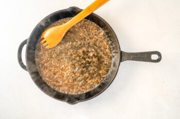 Overhead view of a skillet being deglazed with a wooden spoon.