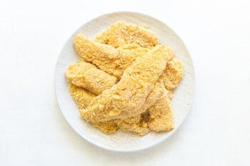 overhead view of breaded chicken tenders before frying on a white plate.