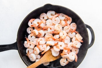 shrimp in a skillet with a wooden spoon.