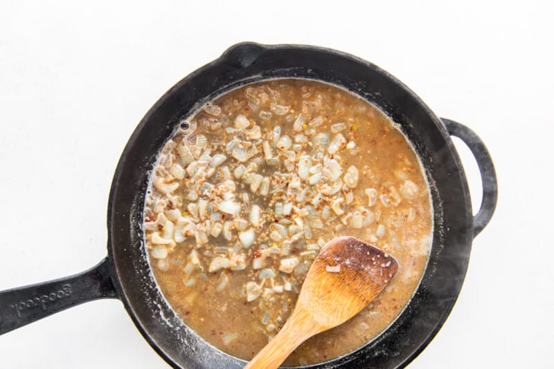 garlic, onions, and white wine in a skillet with a wooden spoon.