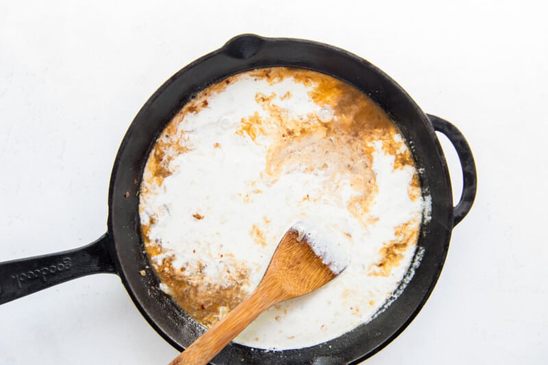 garlic, onions, white wine, and heavy cream in a skillet with a wooden spoon.