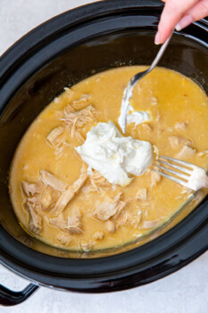 sour cream on chicken and gravy in a crockpot with 2 forks.