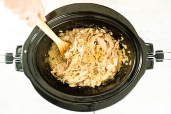 shredded crockpot chicken and rice in a crockpot with a wooden spooon.