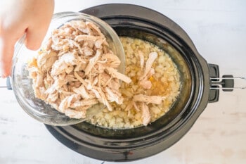 shredded chicken stirred into crockpot chicken noodle soup in a crockpot.