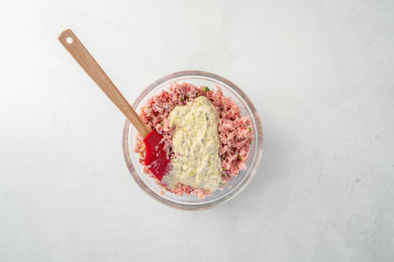 ham salad and mayonnaise sauce in a glass bowl with a rubber spatula.