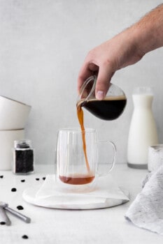 hand pouring espresso into a glass mug