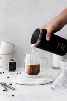 hand pouring frothed milk in a frother into a glass mug