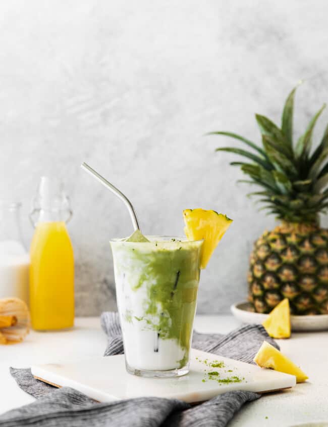 pineapple matcha drink on a white trivet with a stainless steel straw..