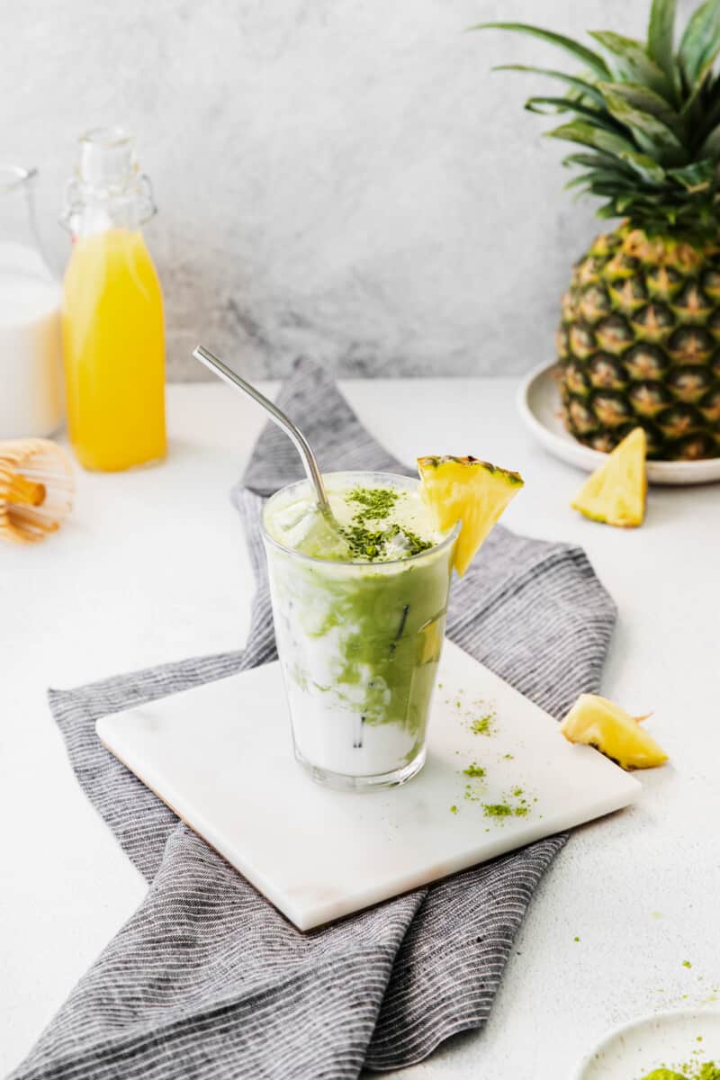 pineapple matcha drink on a white trivet with a stainless steel straw.