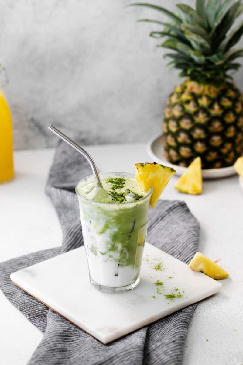 pineapple matcha drink on a white trivet with a stainless steel straw.