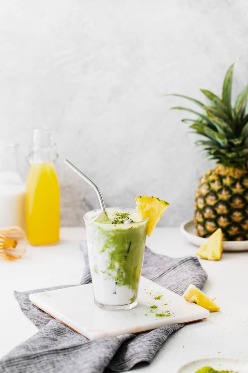 pineapple matcha drink on a white trivet with a stainless steel straw.