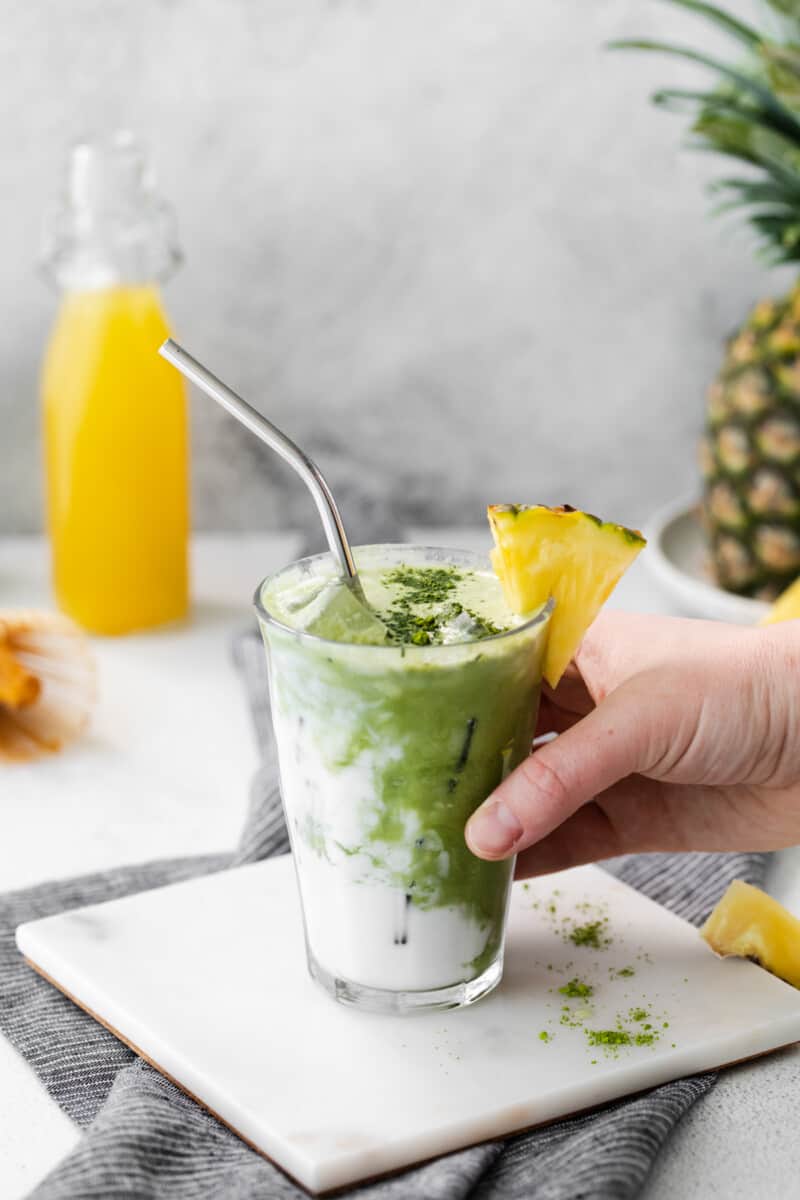 hand grabbing pineapple matcha drink with a stainless steel straw.