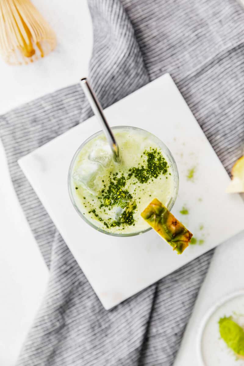 visão aérea da bebida matcha de abacaxi em um tripé branco com um canudo de aço inoxidável.