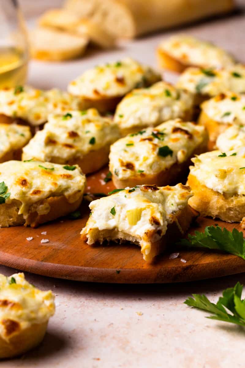 bruschetta topped with artichoke dip on a wooden platter