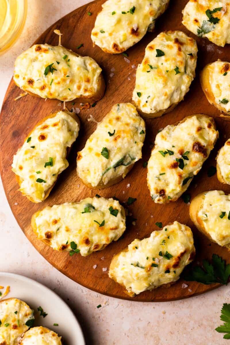 bruschetta topped with artichoke dip on a wooden platter