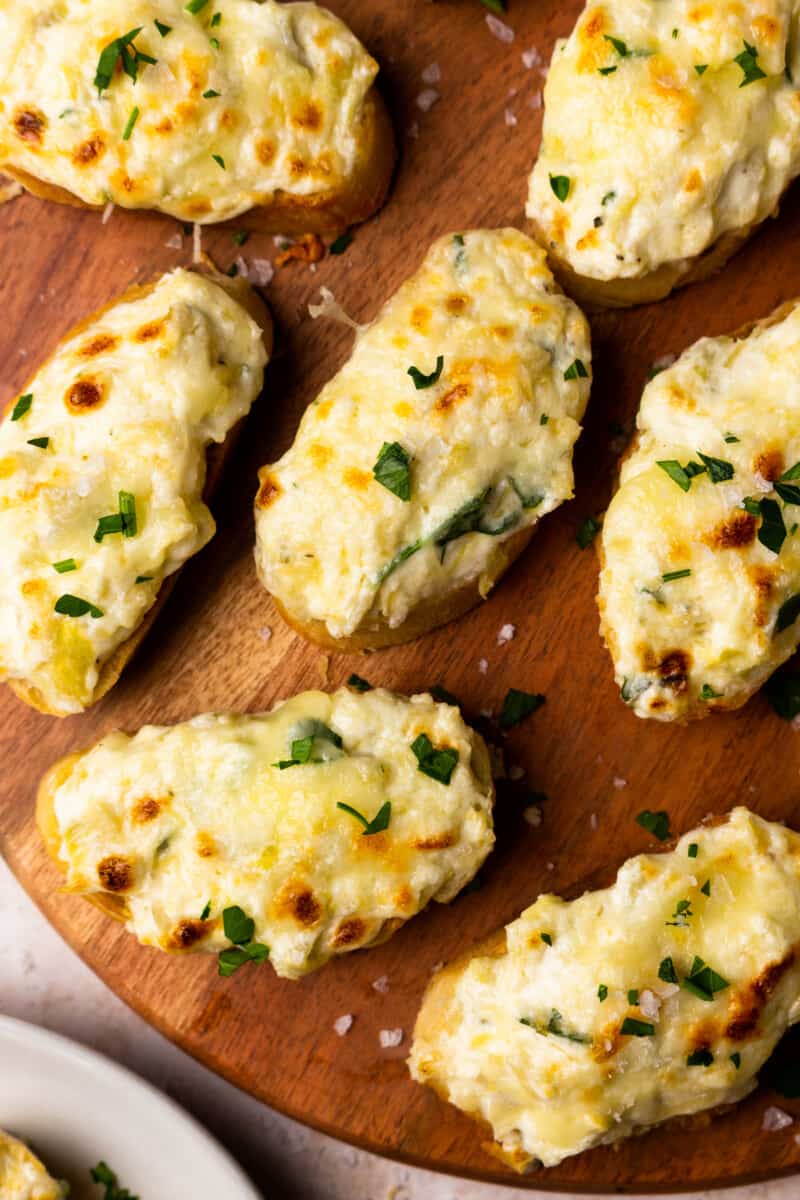 bruschetta topped with artichoke dip on a wooden platter