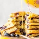 A stack of blueberry pancakes being drizzled with lemon juice and chocolate sauce.