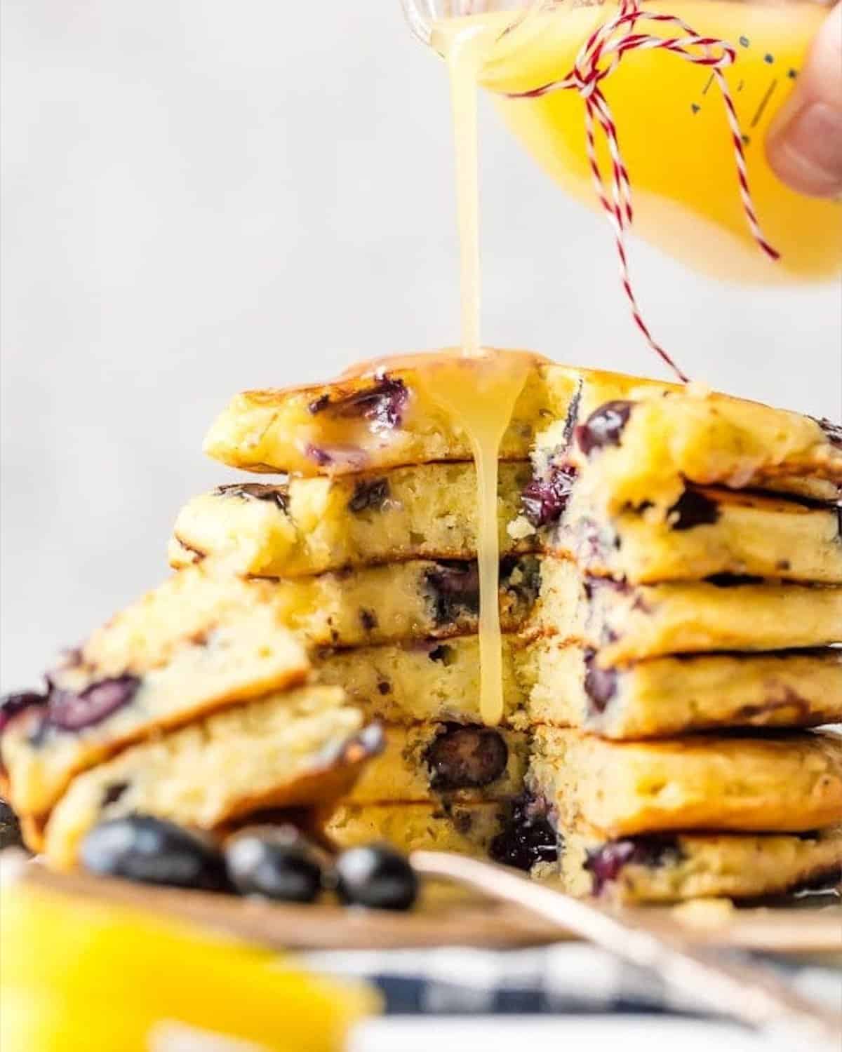 A stack of blueberry pancakes being drizzled with lemon juice and chocolate sauce.