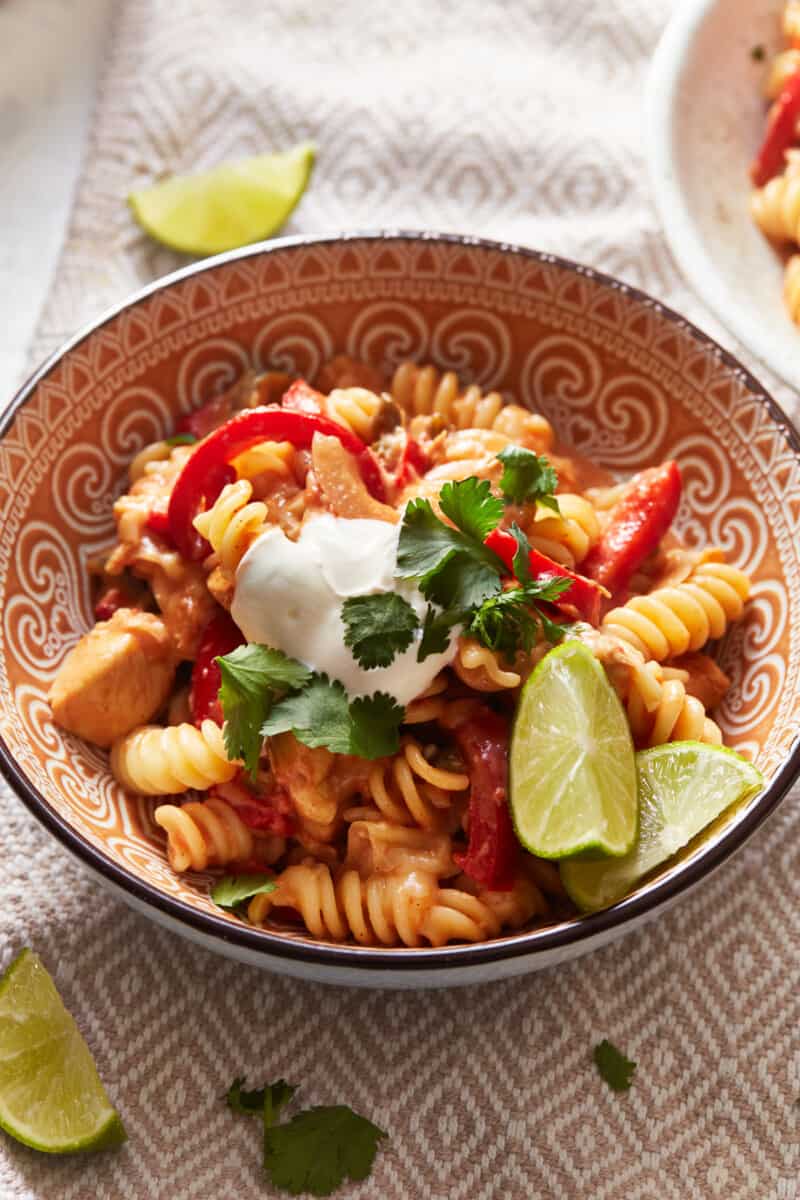 chicken fajita pasta in a patterned bowl with lime wedges.