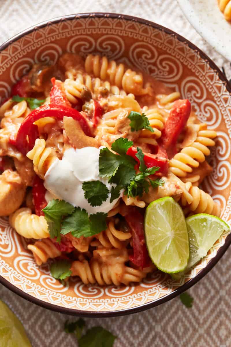 overhead view of chicken fajita pasta in a patterned bowl with lime wedges.