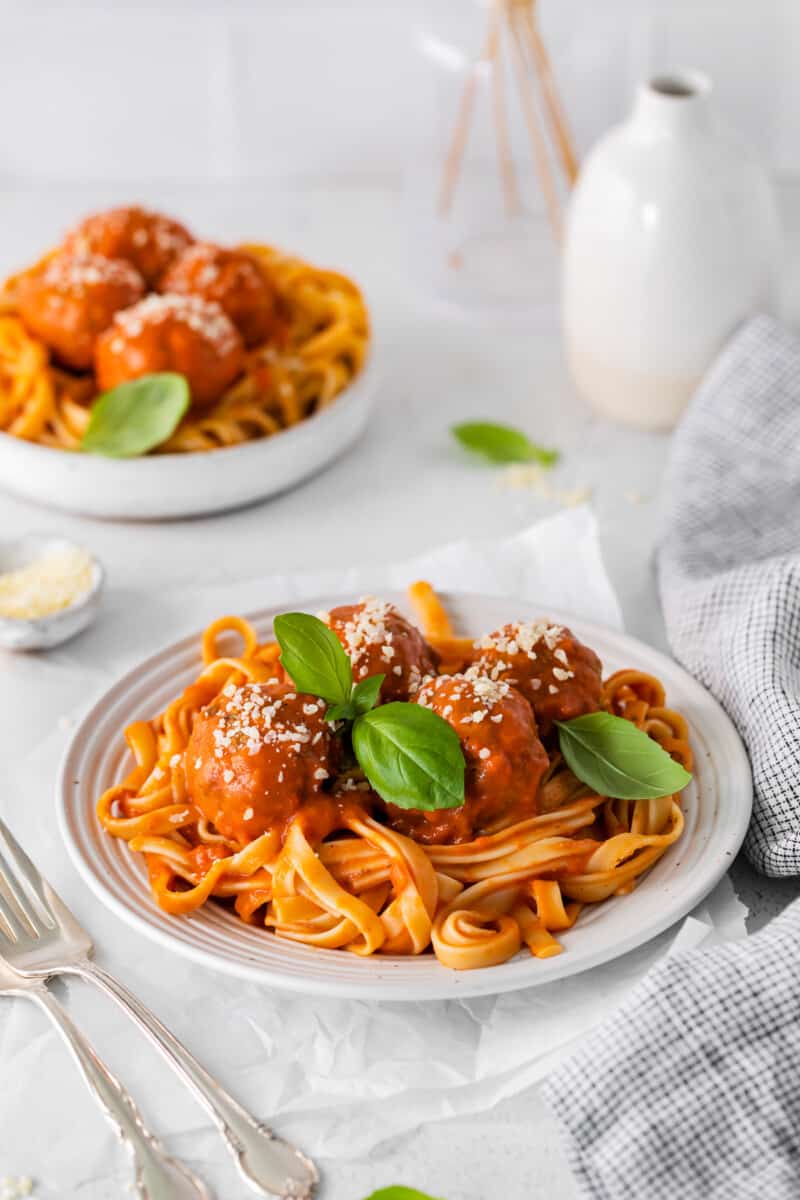 chicken parmesan meatballs over spaghetti in a white bowl with 2 forks.