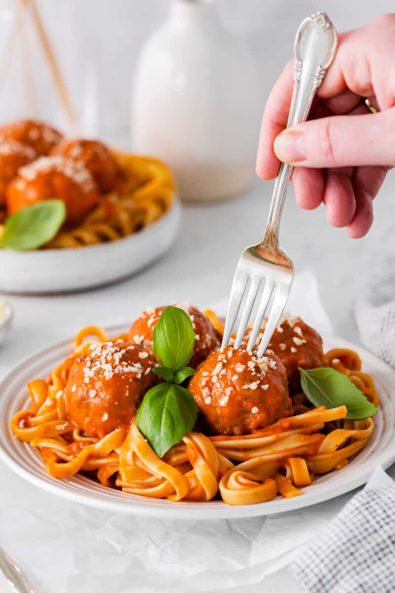 um garfo esfaqueando uma almôndega de frango parmesão sobre espaguete em uma tigela branca.