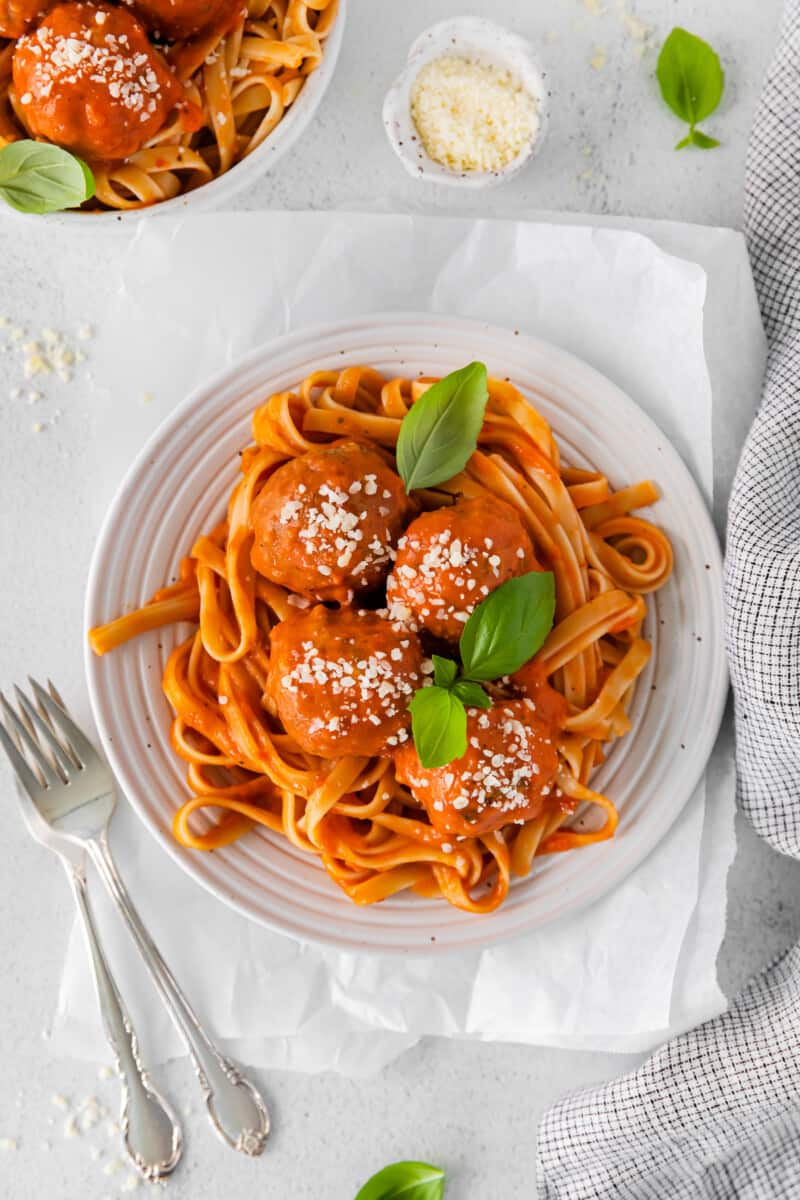 visão aérea de almôndegas de frango parmesão sobre espaguete em uma tigela branca com 2 garfos.