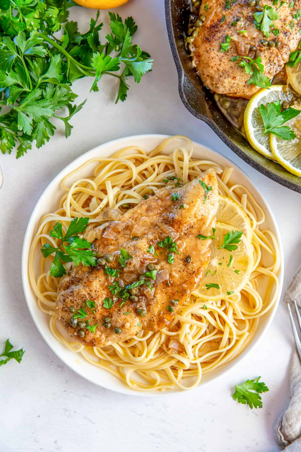 Overhead view of chicken piccata over pasta on a white plate.