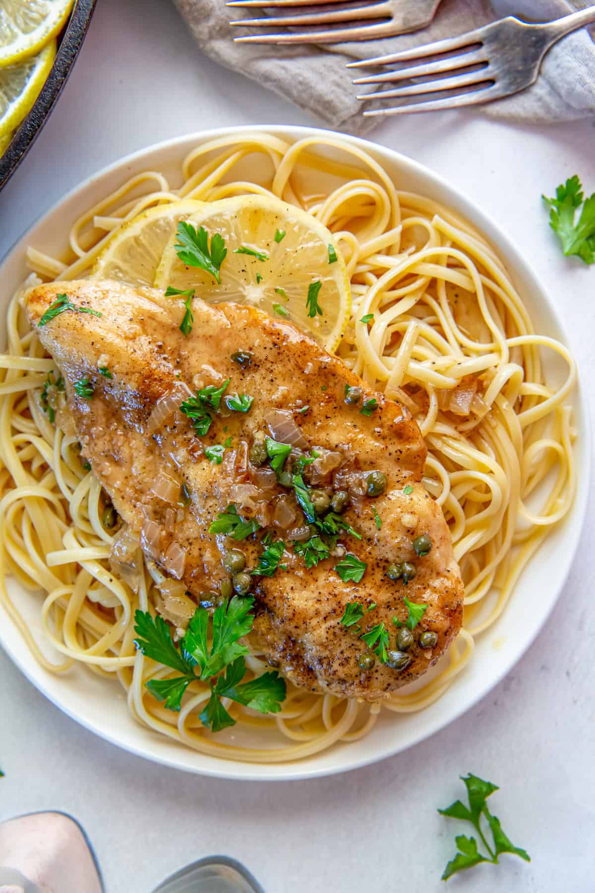 Overhead view of chicken piccata over pasta on a white plate.