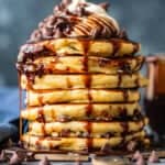 A stack of chocolate pancakes with chocolate syrup and chocolate chips.