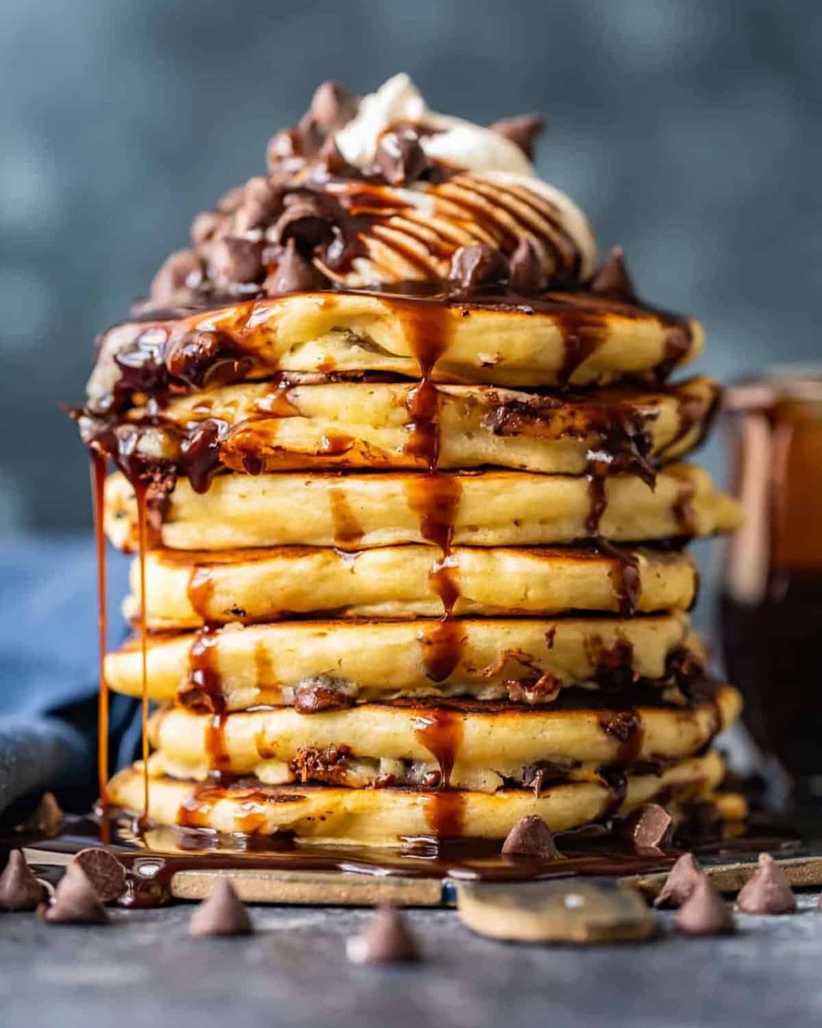 A stack of chocolate pancakes with chocolate syrup and chocolate chips.
