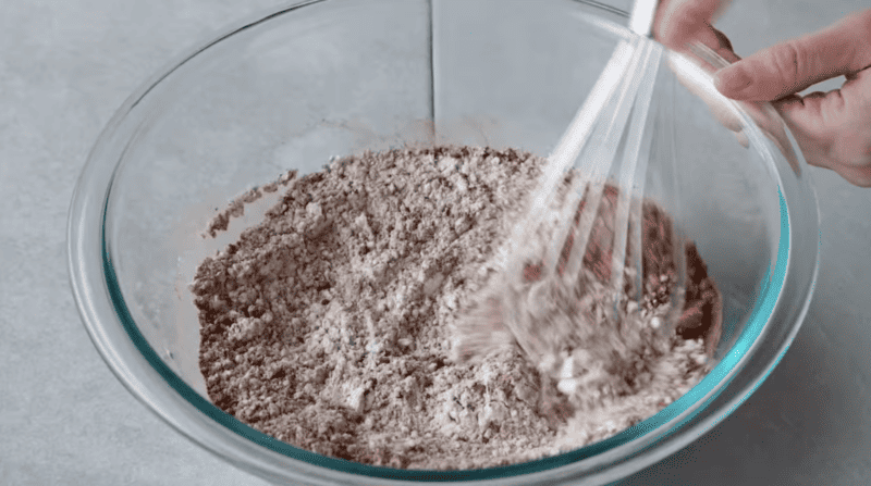 A person mixing flour and chocolate in a bowl to make chocolate pancakes.