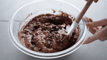 A person mixing chocolate chips into a bowl of pancake batter.