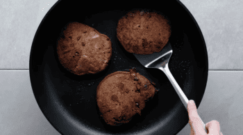 A person is frying chocolate chips in a pan to make delicious chocolate pancakes.
