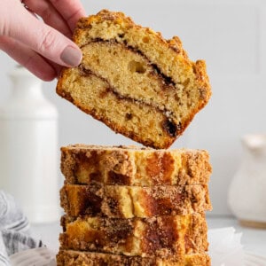 hand grabbing 1 of 5 slices of cinnamon roll bread stacked on a white plate.