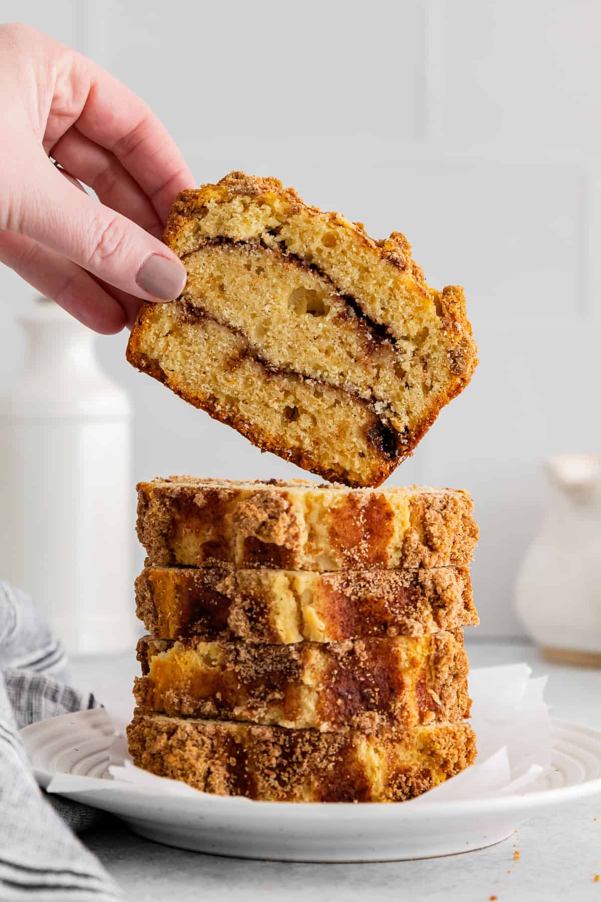 hand grabbing 1 of 5 slices of cinnamon roll bread stacked on a white plate.