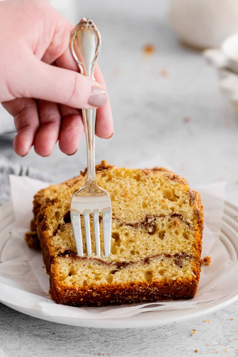 a fork stabbing a slice of cinnamon roll bread on a white plate.